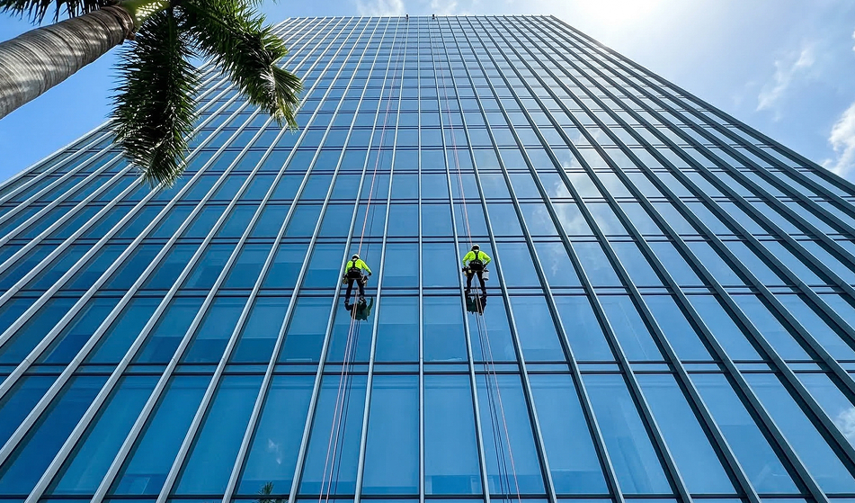 Two rope access technicians working on a glass skyscraper facade seen from street level